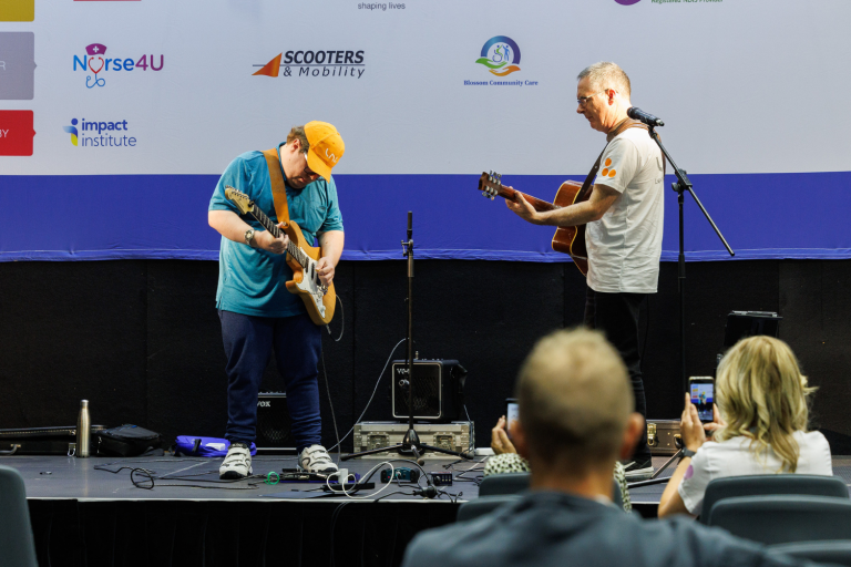 Stage performer playing the guitar with his support worker